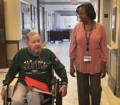 Woman walking alongside male wheelchair user indoors.