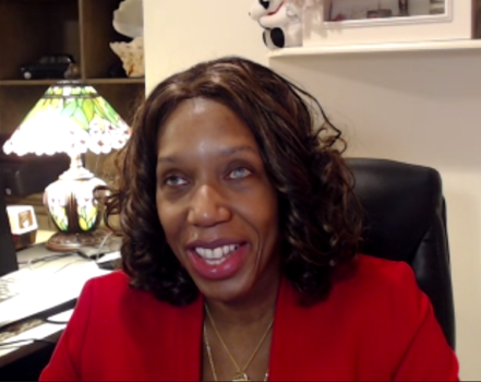 Photo of Sharon McLennon Wier sitting at a desk, wearing a red blazer.