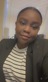 Picture of Karline, an African-American Female with brown eyes and black hair pulled to the back in a bun. Wearing a Black blazer with a black and white striped shirt.