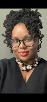 Picture of Shakira, an African American female with brown eyes and glasses, with curly Locs wearing a black knitted shirt with purled black and white Jewelry.