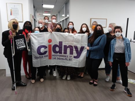 Group of CIDNY staff and German delegation visitors gathered together for a photo holding a CIDNY flag.