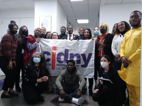 Group of CIDNY staff and African delegation visitors gathered together for a photo holding a CIDNY flag.