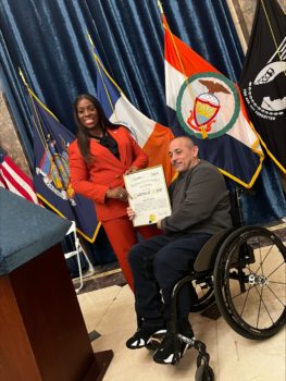 CIDNY's Ramon Santos, using a wheelchair, receives a citation of merit from Bronx Bourgh President Vanessa L. Gibson (standing, dressed in all read) at the Disability Advisory Council Meet & Greet.