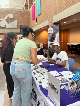 CIDNY staff seated at a table full of informational materials speaks to attendees.
