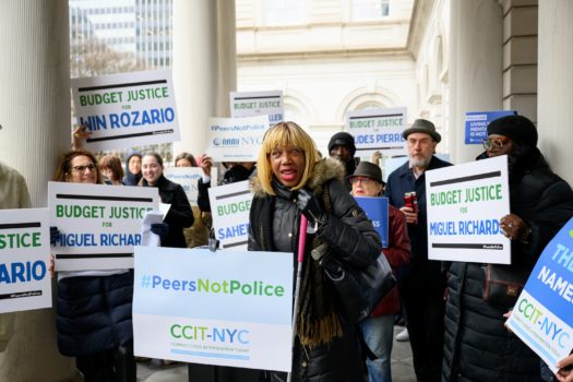 CIDNY's Dr. Sharon McLennon Wier speaks at a Peers Not Police rally surrounded by advocates holding signs.