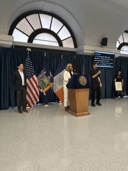 CIDNY's Dr. Sharon McLennon Wier at a lecturn, speaks at the 2025 Manhattan Disability Pride Event, with an ASL interpreter alongside.