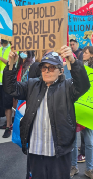 Michael Schweinsburg holding a sign at a rally that says "Uphold Disability Rights"