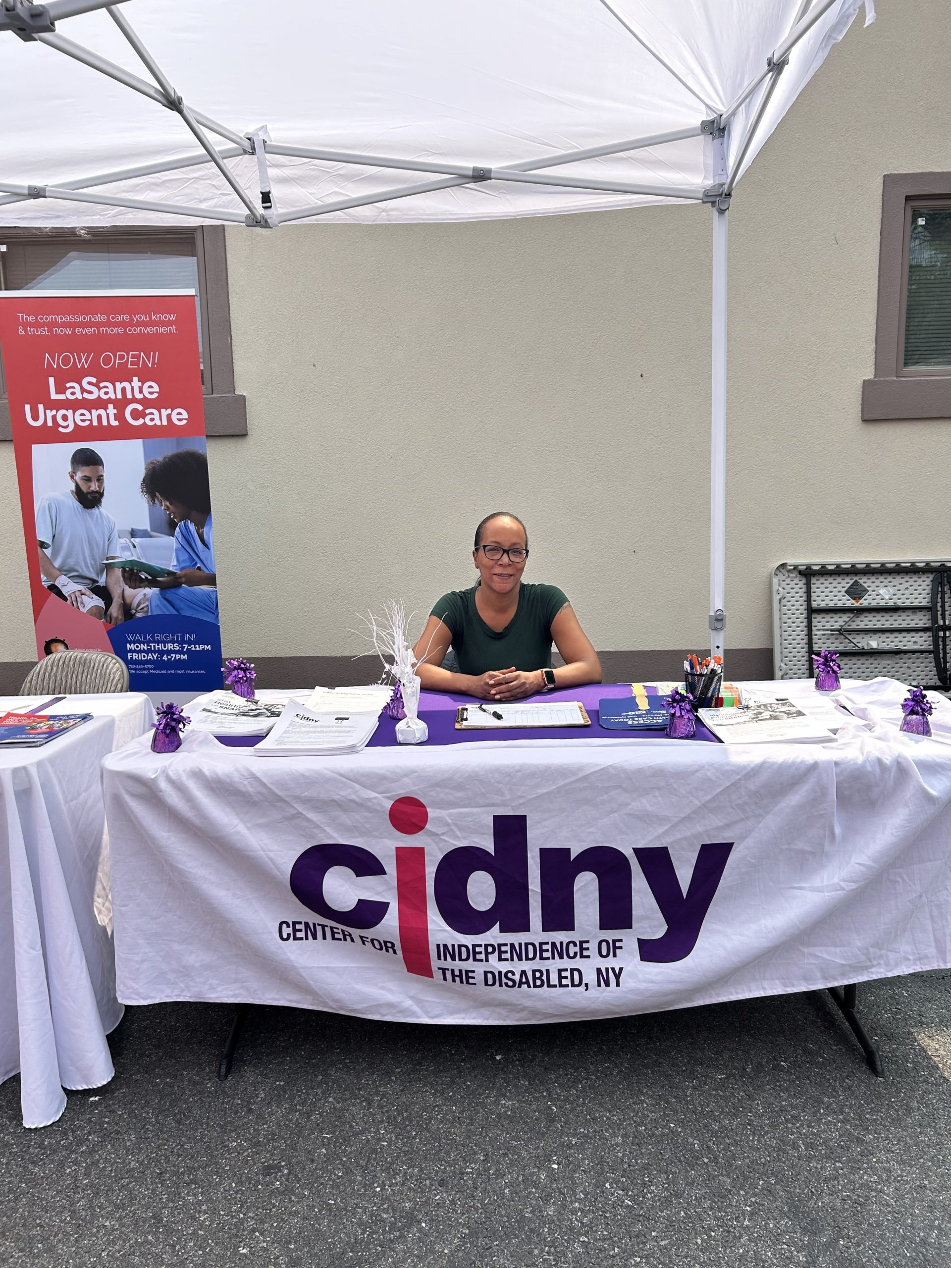 A CIDNY team member sits at a table with a cidny logo on it with NOEP materials.