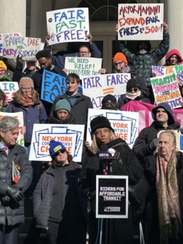 Dr. Sharon McLennon Wier, backed by advocates holding signs, speaks on the steps of City Hall regarding transit access and equity.